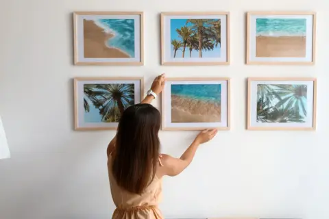 Frau arrangiert Bilder mit Strandmotiven. Tolle bilder anordnen ideen für eine sommerliche Wandgestaltung.