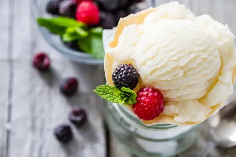 Cremiges Joghurteis selber machen: Eine Portion mit frischen Beeren und Minze garniert, daneben eine Schüssel voller Beeren.