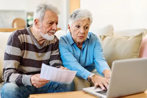 Couple âgé discutant de l'habilitation familiale et du placement en EHPAD, l'un tenant des papiers, l'autre sur un ordinateur portable.
