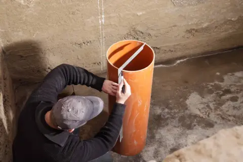 Mann markiert Rohr für Pumpensumpf im Keller.