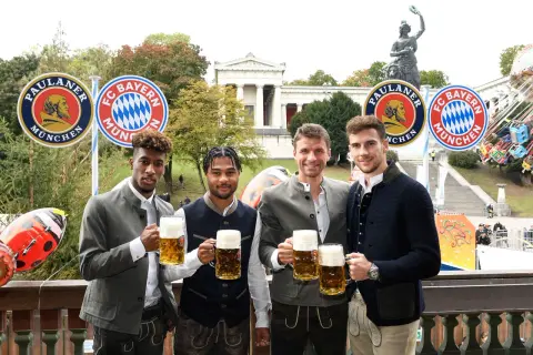 Vier FC Bayern Spieler in Tracht mit Bierkrügen, vor Paulaner- und FC Bayern-Logos. Ein Fest für alle Fans bei Veranstaltungen in Bayern.