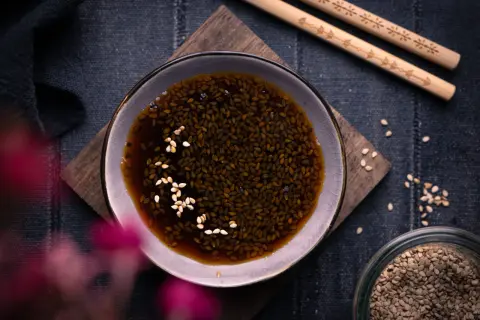Schale mit Teriyaki-Sauce und Sesam, daneben Stäbchen und ein Glas Sesamsamen. Perfekt für dein Teriyaki Sauce Rezept!