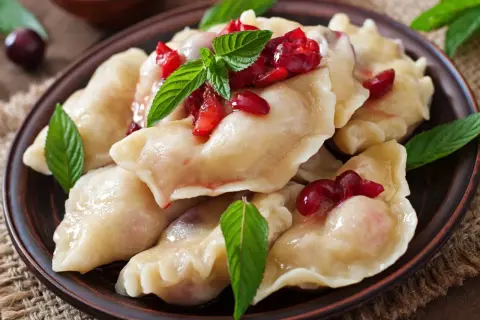 Pyszne, domowe ciasto na pierogi pieczone w piekarniku, podane z wiśniami i miętą.