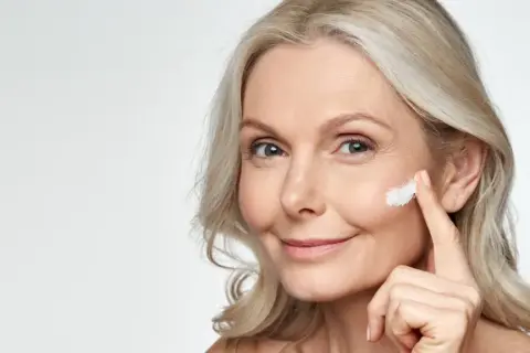 Eine Frau trägt Sonnencreme auf, um Falten vorzubeugen. Jeden Tag Sonnencreme gegen Falten schützt die Haut.