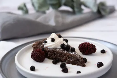 En bit vegansk kladdkaka med vispad grädde och bär.