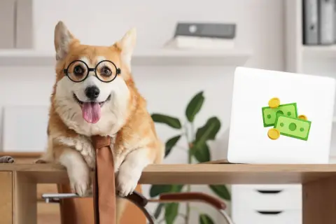En glad hund på kontoret med glasögon och slips. Bredvid en laptop med penga-symboler.