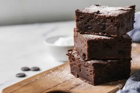 Pyszne, wilgotne brownie z kawałkami czekolady, posypane cukrem pudrem. Idealne na deser według prostego brownie przepisu.
