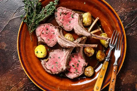 Costolette di agnello in padella, succulente e rosate, servite con patate novelle arrosto e rametti di timo su un piatto di terracotta.