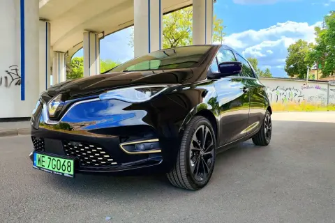 Czarny Renault Zoe błyszczy pod betonowym wiaduktem. Ten elektryczny samochód oferuje imponujący zasięg, idealny na miejskie podróże i dalsze wyprawy.