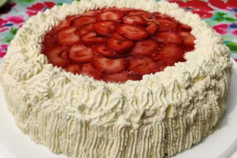 En vacker jordgubbstårta med fluffigt gräddtäcke och ett glansigt jordgubbslager i mitten. Denna ser ut att vara den godaste jordgubbstårtan!