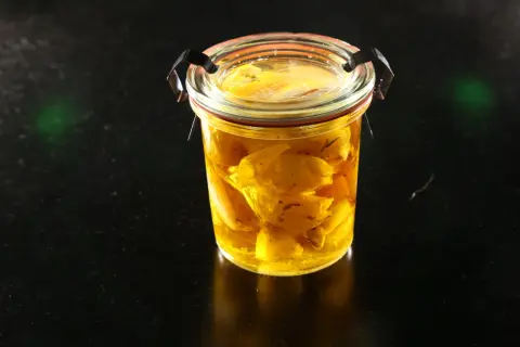 Un bocal en verre rempli d'ail confit dans de l'huile dorée. Les bienfaits de l'ail confit sont nombreux pour la santé.