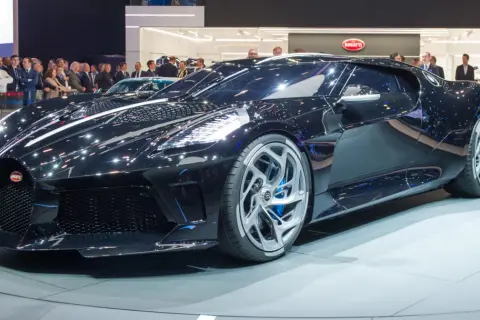 Lśniący, czarny Bugatti La Voiture Noire na wystawie, otoczony tłumem widzów.