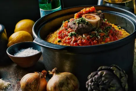 En mustig risotto milanese med en saftig köttbit och tomatsås, omgiven av citroner, lök och kronärtskocka.