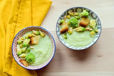 Zwei Schalen cremiger Gemüsesuppe, garniert mit Romanesco, Croutons und Pinienkernen. Ein köstliches Romanesco-Rezept für kalte Tage.
