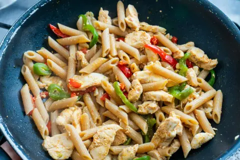 Makaron penne z kurczakiem i papryką w czarnej patelni.