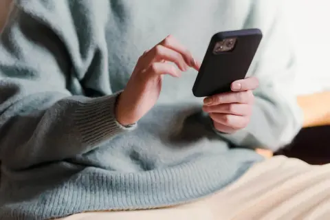 Dłonie trzymające telefon, zastanawiające się, co napisać po kłótni.