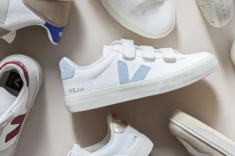 Plusieurs baskets Veja blanches, certaines avec des touches de couleur, sont disposées sur un fond clair. Idéal pour apprendre comment nettoyer des baskets.
