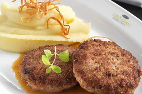 Zwei saftige faschierte Laibchen mit cremigem Kartoffelpüree und knusprigen Röstzwiebeln, garniert mit frischen Kräutern.