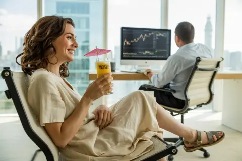 Kobieta z drinkiem i parasolką obserwuje wykresy na monitorze, podczas gdy mężczyzna pracuje. Czy trading jest legalny? Tak, a wyniki mogą być relaksujące.