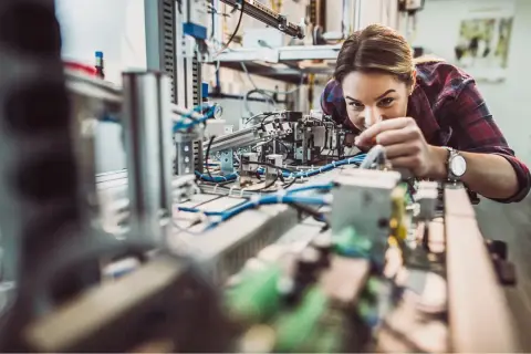 Junge Frau arbeitet konzentriert an einer komplexen Anlage im Bereich IU Elektrotechnik.