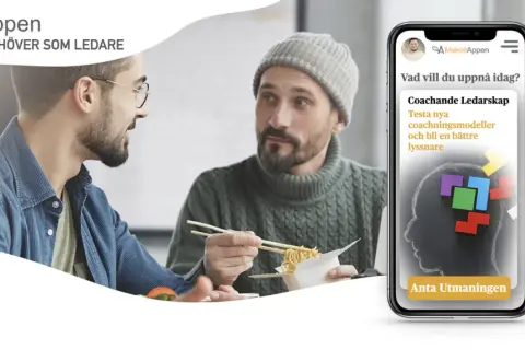 Två män äter lunch och pratar. En mobil visar appen MakeitAppen med en utmaning för coachande ledarskap, ett bra sätt att visa uppskattning på jobbet.
