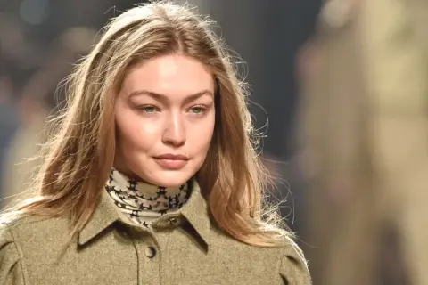 Modelo con cabello rubio y mechas blancas, viste una chaqueta verde y un pañuelo estampado.