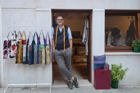 Uomo con metro da sarto nel suo atelier a Venezia. Borse colorate in esposizione.