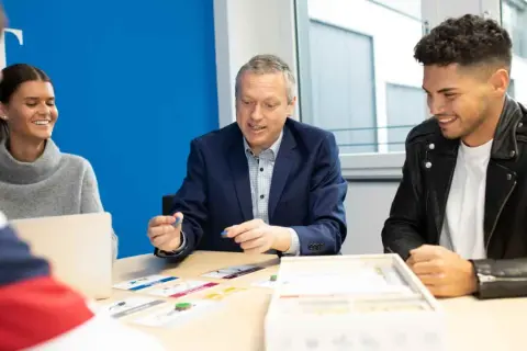 Ein Mann erklärt jungen Leuten beim dualen Studium Marketing Berlin ein Spiel.