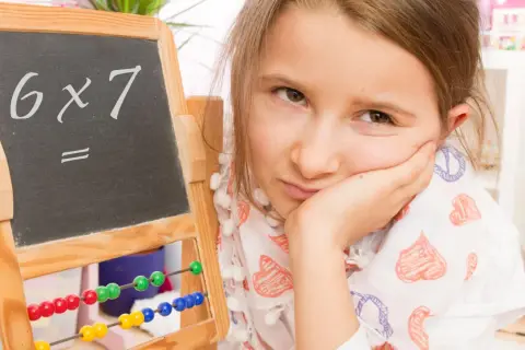 Mädchen mit gelangweiltem Gesichtsausdruck vor einer Tafel mit "6x7=". Vielleicht hilft die Trachtenberg-Methode beim Rechnen.