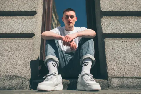 Młody mężczyzna w jeansach i białej koszulce prezentuje modne **wysokie skarpetki stylizacje**.