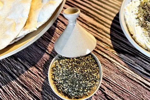 Un bol de zaatar prêt à être utilisé pour une recette, avec du pain pita et une trempette crémeuse.
