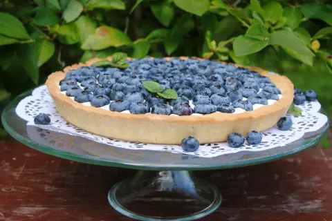 Pyszna tarta z borówkami, udekorowana listkami mięty, prezentuje się apetycznie na szklanej paterze.
