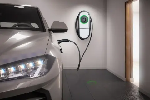 Auto elettrica in ricarica in un box privato. Stazione di ricarica a muro e cavo collegato. Luce verde sul pavimento indica la posizione.