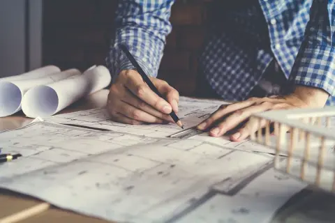 Architetto disegna progetto, con rotoli di carta e modello edilizio. Lavora per ottenere il permesso di costruire in sanatoria.