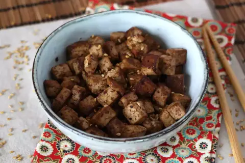 En skål med krispiga, tärnade tofu bitar, glaserade i en smakrik, glutenfri marinad och toppade med sesamfrön.