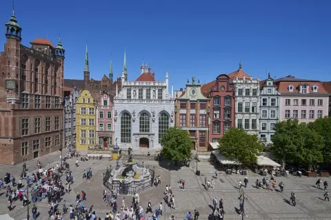 Tętniący życiem gdański plac z Dworem Artusa, fontanną Neptuna i kolorowymi kamieniczkami.