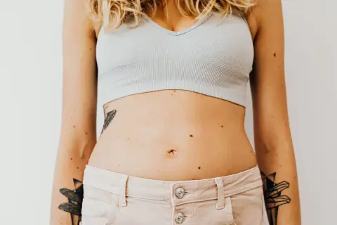 En kvinna med tatueringar på armarna och magen, som visar sin mage som kan vara känslig för gluten.