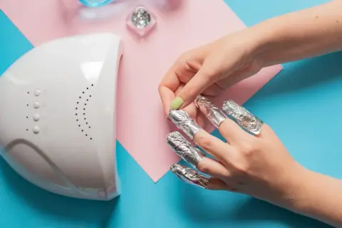 Rimozione smalto semipermanente: unghie avvolte in stagnola, lampada UV e glitter. Attenzione, il semipermanente rovina le unghie se non rimosso correttamente.