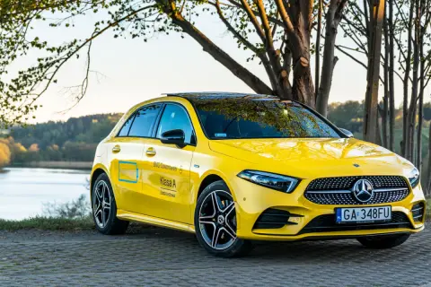 Żółty Mercedes A250 z czarnym dachem i felgami, zaparkowany nad jeziorem.