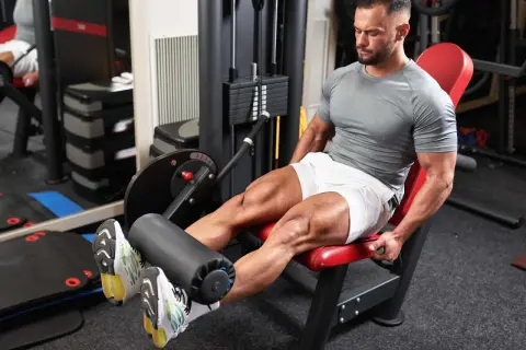 Mann trainiert den Beinstrecker Muskel an einem Gerät im Fitnessstudio.