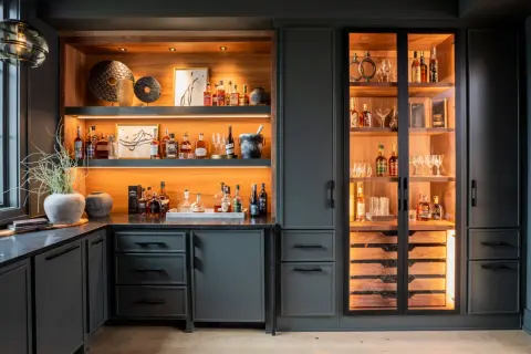 Stylish basement bar ideas featuring illuminated shelves stocked with liquor bottles, glassware, and decorative items.