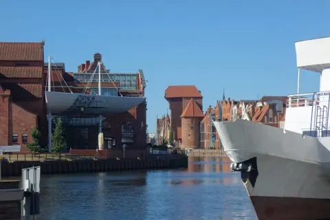 Widok na Motławę podczas weekendu w Gdańsku. Biały kadłub statku na pierwszym planie, w tle zabytkowe kamieniczki i Żuraw.