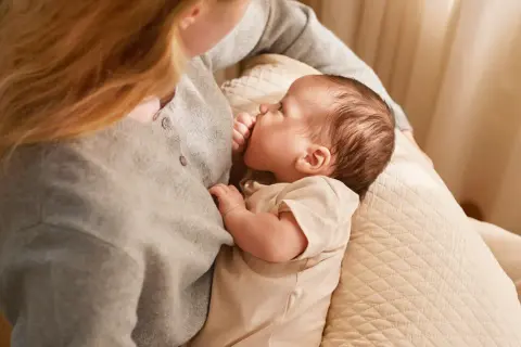 En mamma ammar sin bebis, som är cirka 6 veckor gammal. Mjukt ljus faller in från sidan.