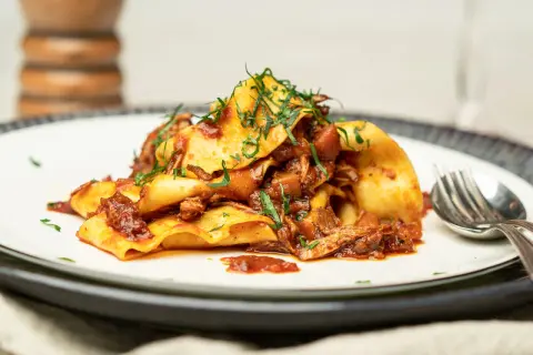 Herzhaftes Pasta Ragu mit breiten Nudeln, übergossen mit einer reichhaltigen Fleischsauce und garniert mit frischen Kräutern.