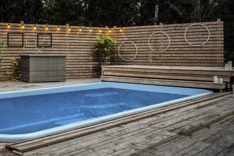 En avkopplande oas med en pool omgiven av en vacker trall. Ljusslingor och dekorationer skapar en mysig atmosfär.