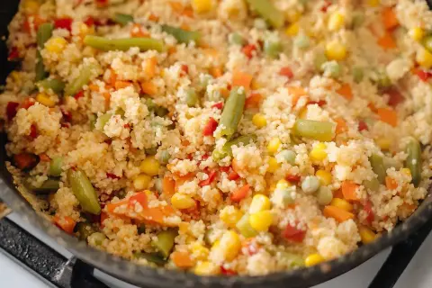 En varm och färgglad couscousrätt med gröna bönor, majs, morötter och paprika i en stekpanna.