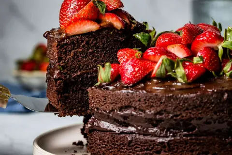 Ein hoher Schokokuchen mit frischen Erdbeeren und Schokoladenglasur wird angeschnitten.