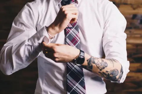 Mężczyzna w białej koszuli i krawacie poprawia mankiet, odsłaniając tatuaż na ramieniu. Czy prawnik może mieć tatuaż? Tak!