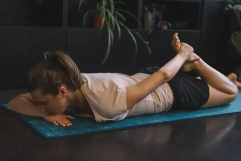 Femme pratiquant des exercices de yoga pour soulager la cruralgie, en position de cobra inversé sur un tapis bleu.