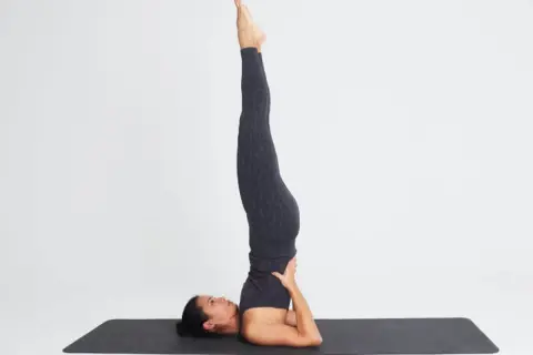 Mujer en postura de yoga invertida. Considera las contraindicaciones de las posturas invertidas en yoga antes de practicar.
